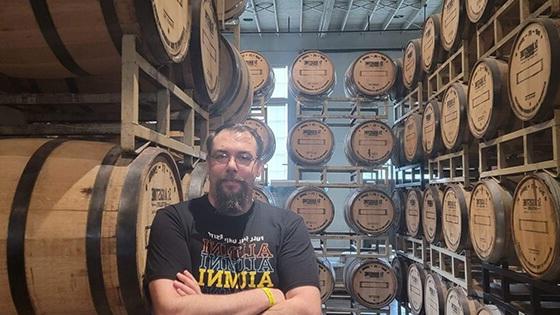 Daniel Vanallen sits in a chair at St. Augustine Distillery Co. He is smiling and wearing a Full Sail Alumni shirt.